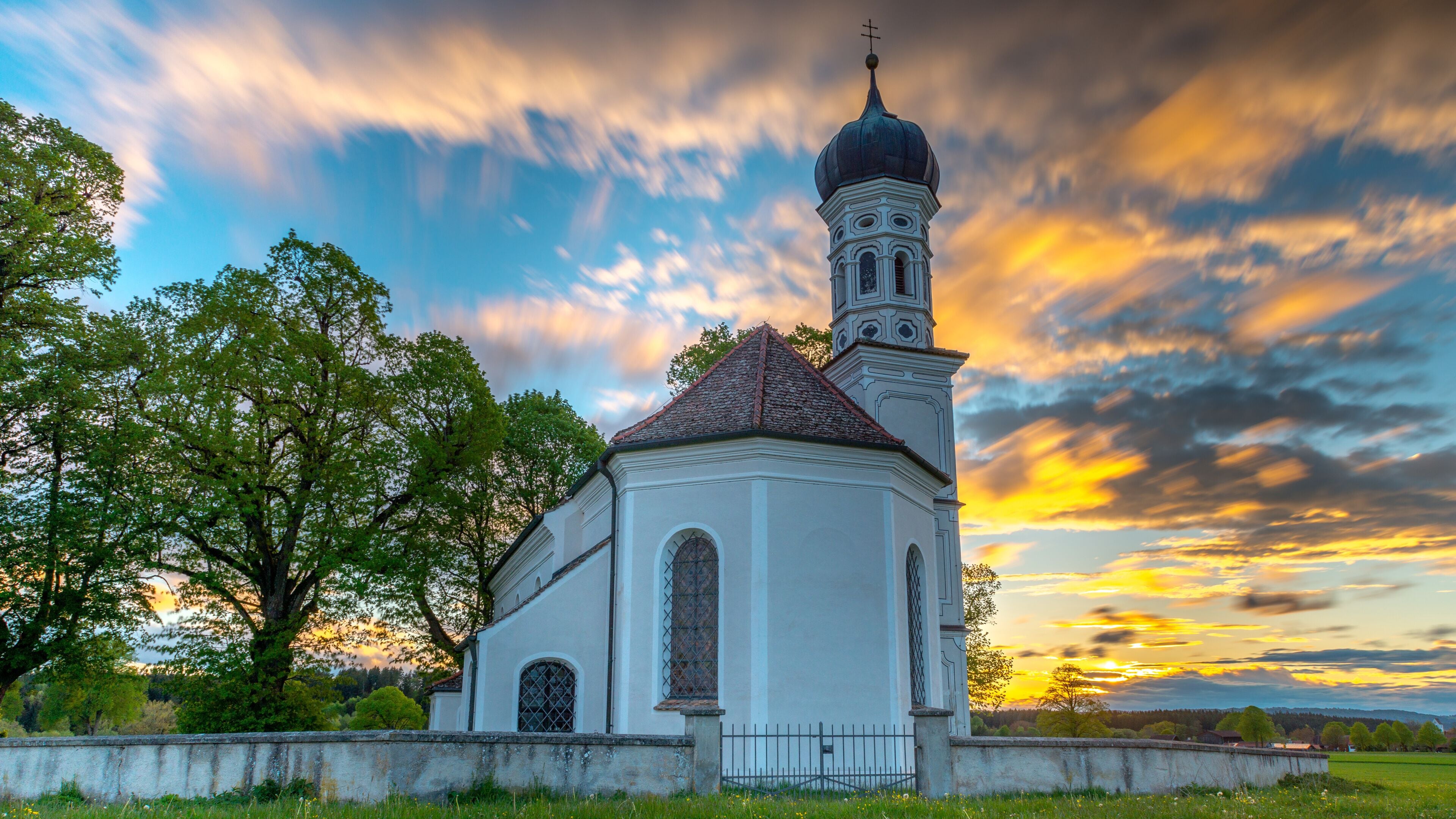 A white church with a bell tower and a large tree in the foreground.