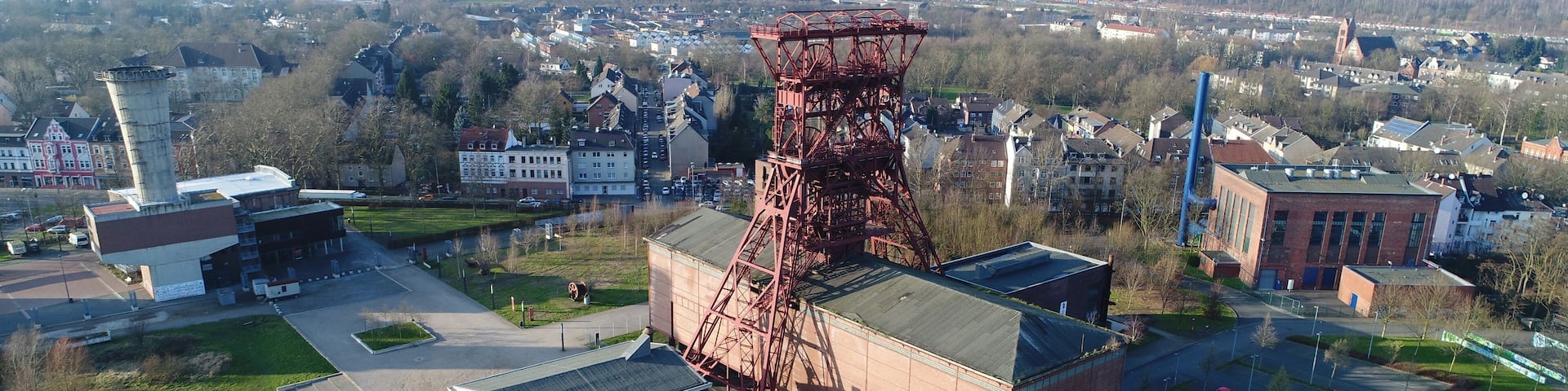 An aerial view of a cityscape with a prominent red industrial tower, a large brick building, and a green park area.