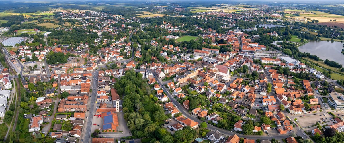 An aerial view of a town with red-roofed houses, a river, and surrounding green fields.