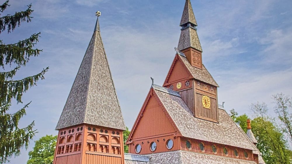 Une église dotée d’un clocher imposant et d’une tour plus petite, entourée de verdure.