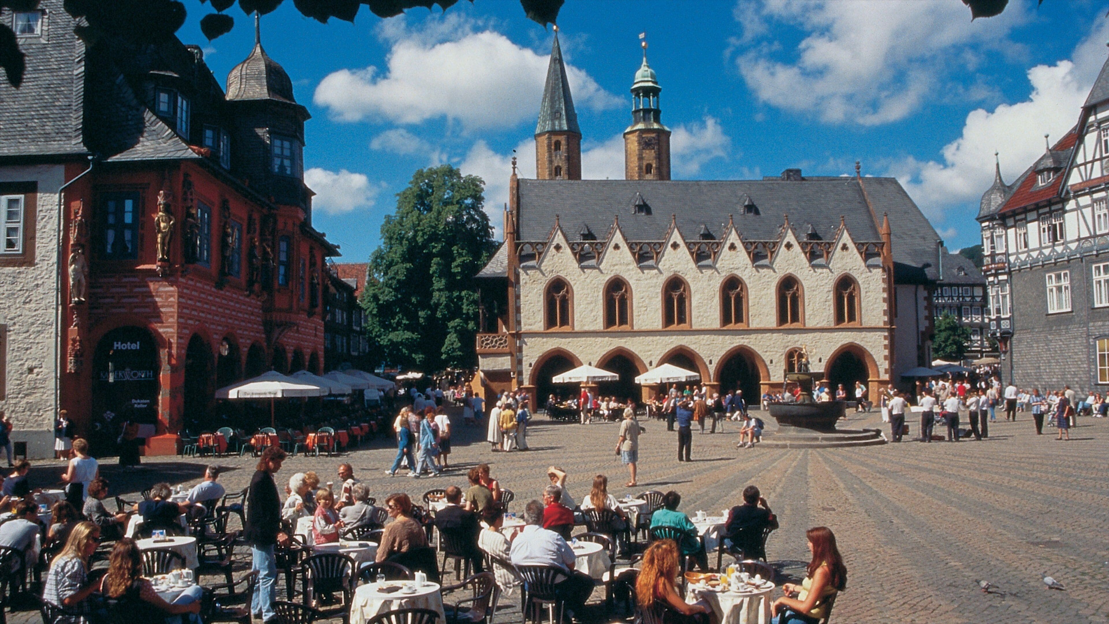 A bustling square with historic buildings, a prominent church with a tall spire, and outdoor cafes.