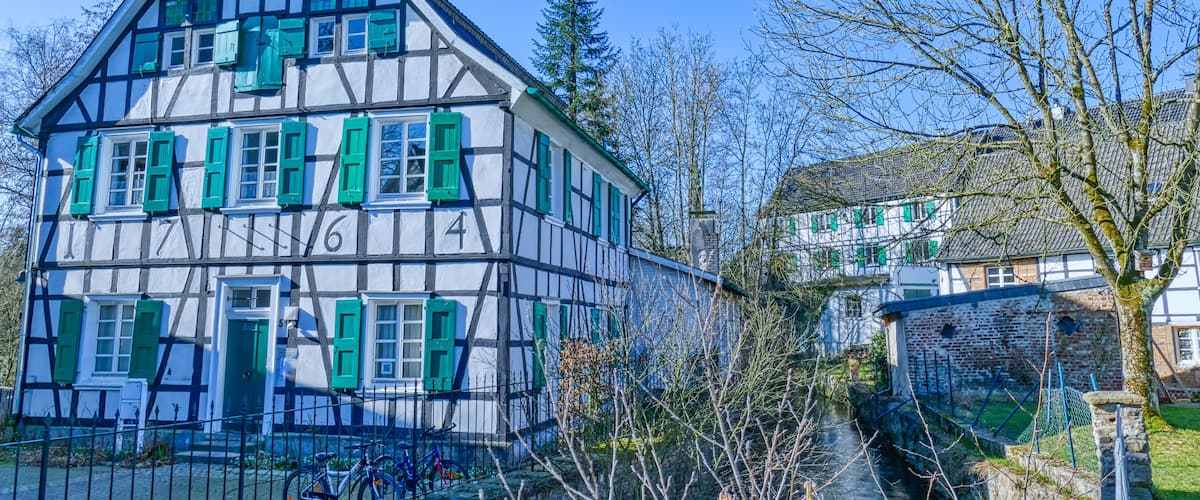 A traditional half-timbered house with green shutters, a canal, and a bicycle.