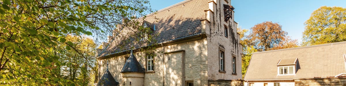 A historic stone building with a turret, a cobblestone pathway, and a tree-lined canal.