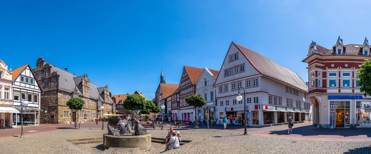 A cobblestone square with historic buildings, a fountain, and a clear blue sky.