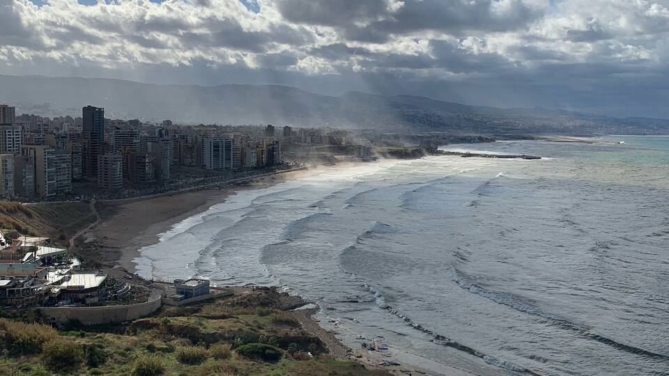 Paisagem costeira com praia, edifícios e palmeiras.