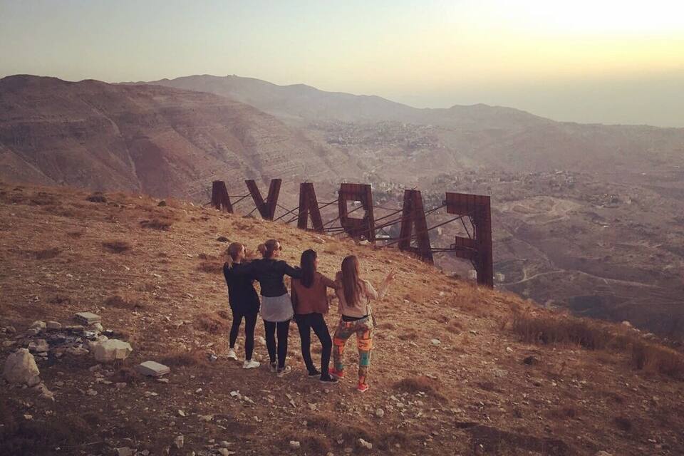 A group of people standing on a hill with a large wooden sign that reads "FARAVAN".