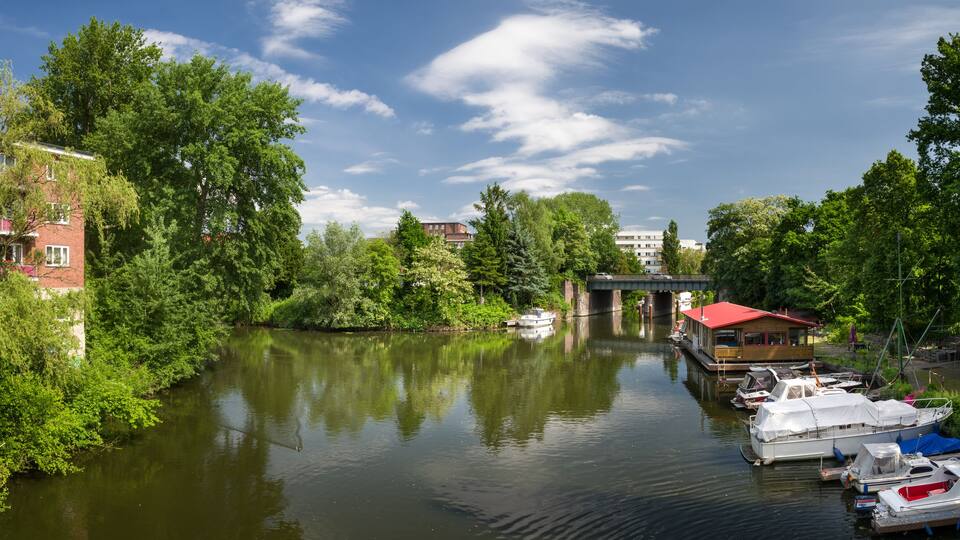 A river with boats docked, surrounded by lush greenery and buildings.