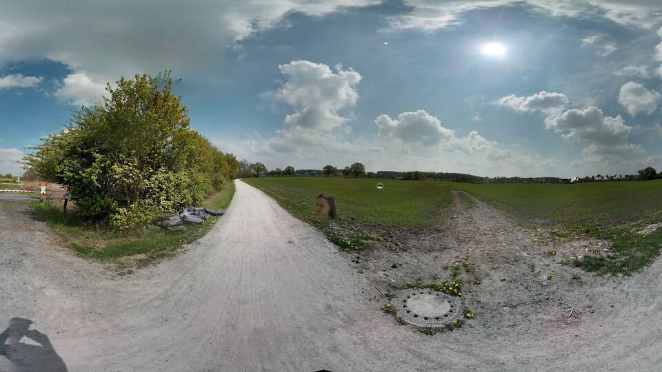 A rural road flanked by trees and fields under a partly cloudy sky.