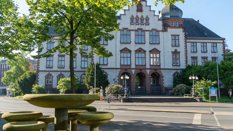 A historic building with arched windows and a dome, surrounded by trees and a fountain.