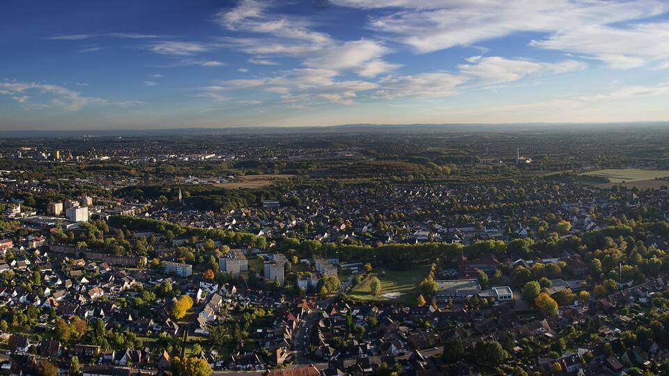 A cityscape with a mix of residential and commercial buildings, surrounded by greenery and a clear sky.