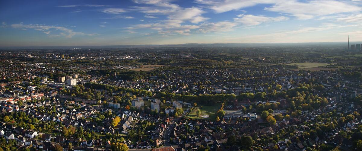 A cityscape with a mix of residential and commercial buildings, surrounded by greenery and a clear sky.
