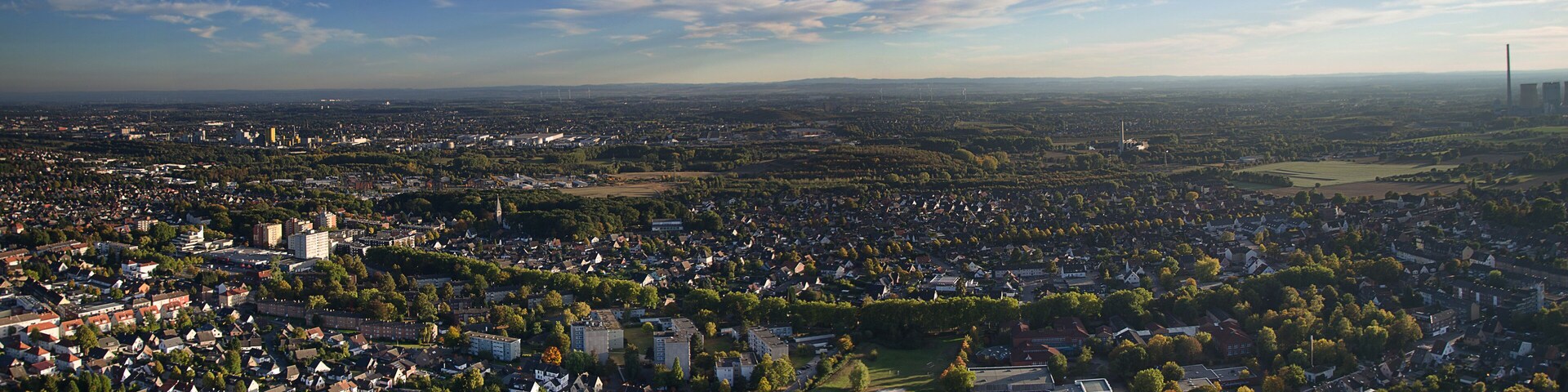 A cityscape with a mix of residential and commercial buildings, surrounded by greenery and a clear sky.