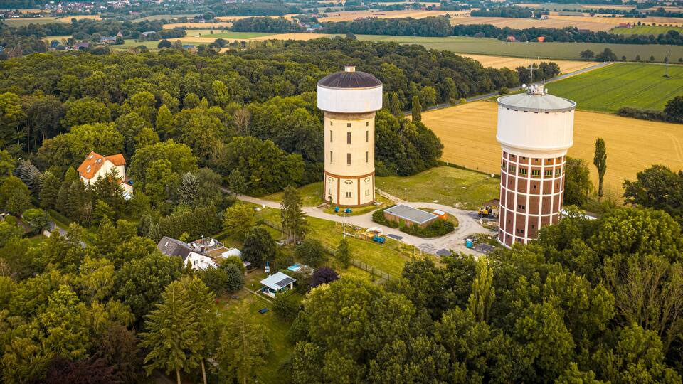 Two water towers surrounded by lush greenery and fields.