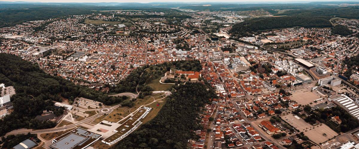 An aerial view of a densely populated city with a mix of residential and commercial buildings, surrounded by green hills and a large open area.