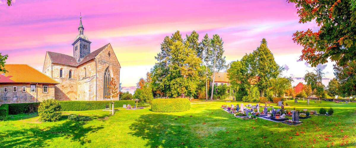 A church with a steeple, a cemetery, and surrounding trees.