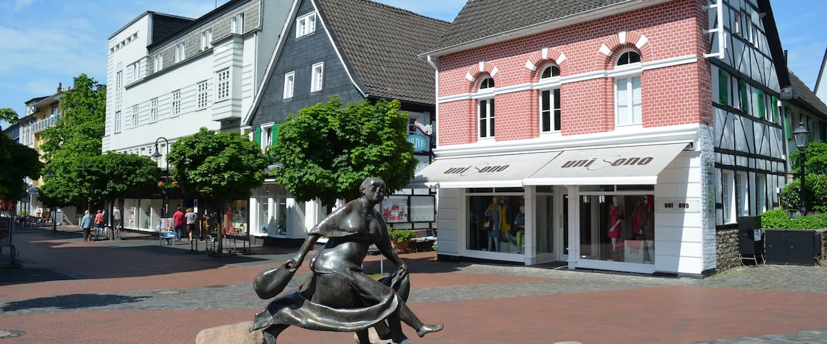 A cobblestone square with a statue, historic buildings, and a boutique store.