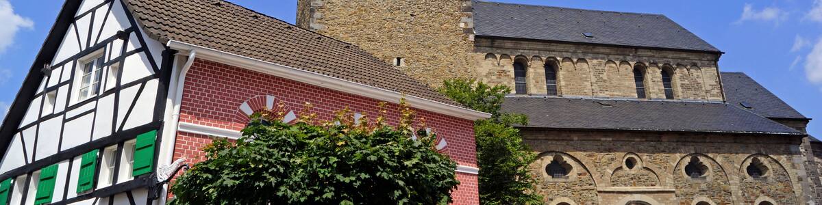 Eine Kirche mit hohem Turm und einem Fachwerkhäuschen davor.