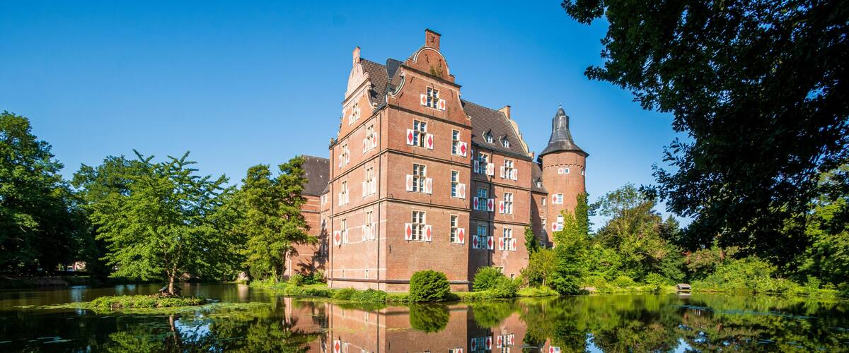 A historic building with a tower, surrounded by a calm lake with lily pads, and lush greenery.