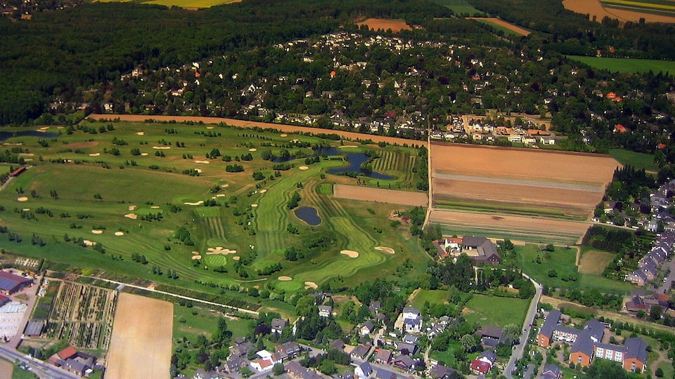 An aerial view of a rural area with a golf course, residential houses, and agricultural fields.