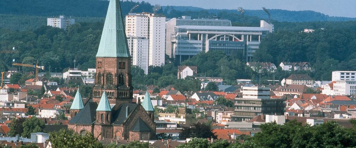 A cityscape with a prominent church with a green spire, surrounded by residential buildings and a modern high-rise building in the background.