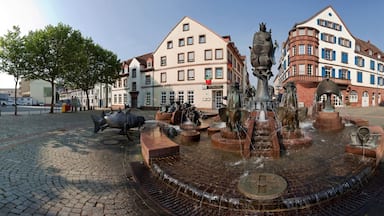 Une fontaine historique ornée de statues, entourée d’un pavage en pierre et de bâtiments traditionnels.