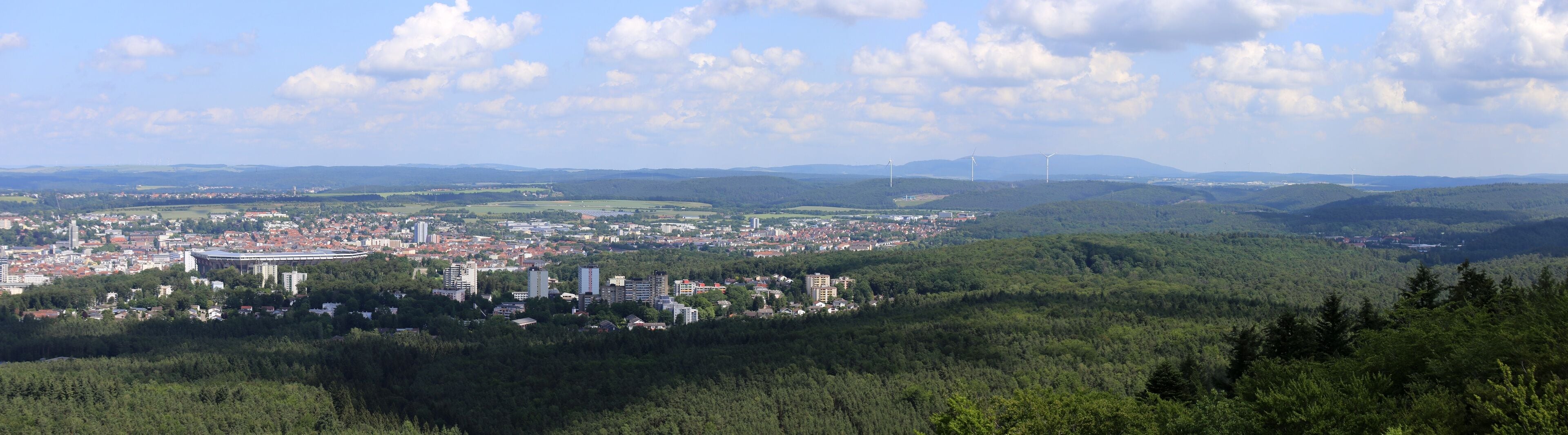 A city nestled in a valley with rolling hills and wind turbines in the distance.