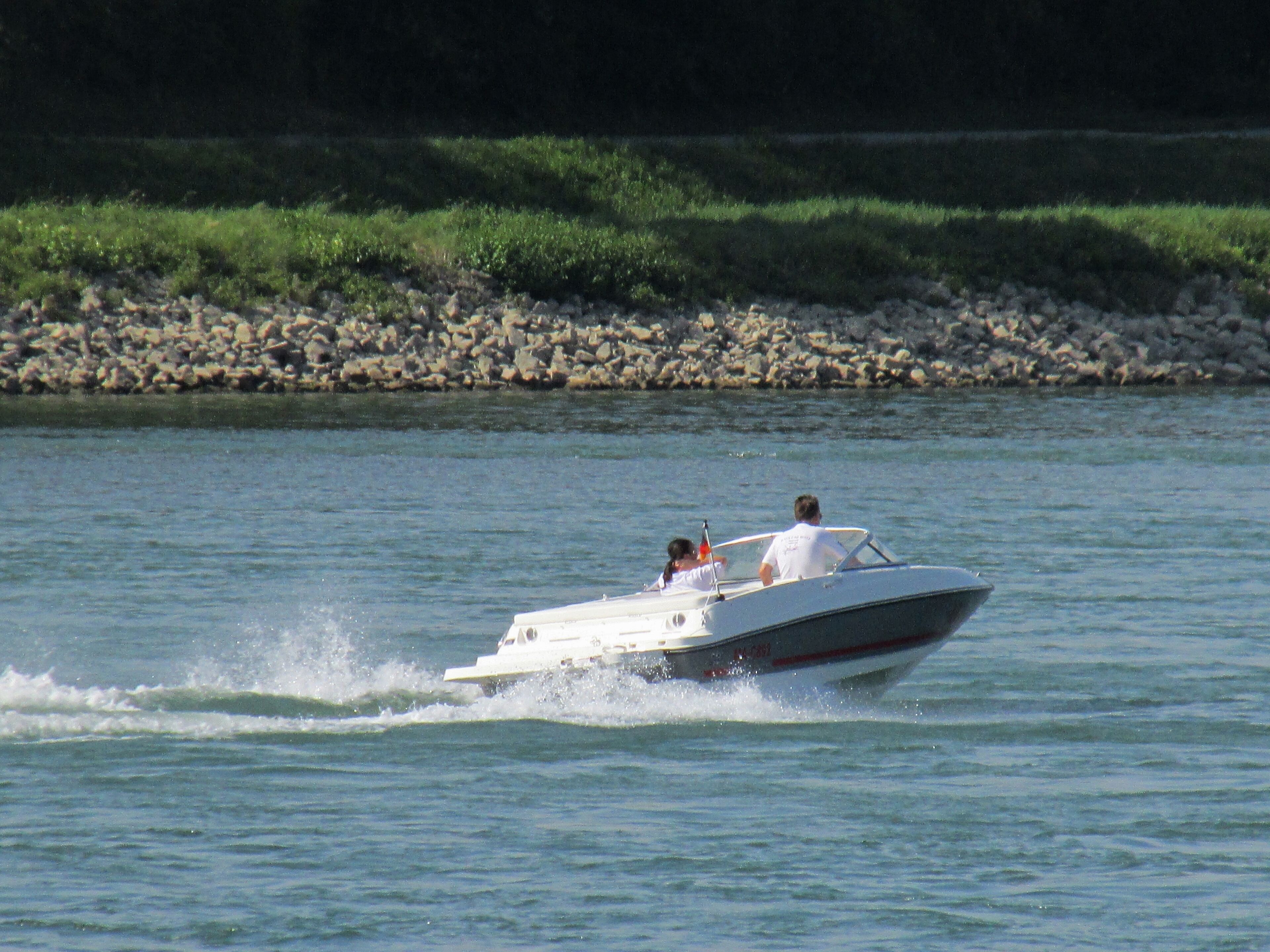 A speedboat with two people on the water near a rocky shore.