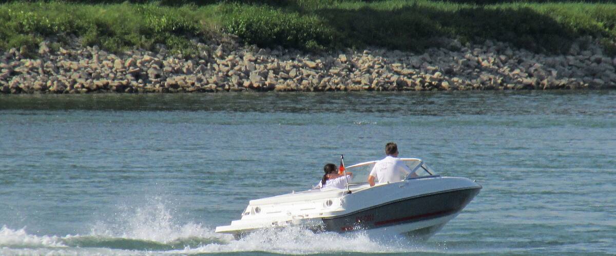 A speedboat with two people on the water near a rocky shore.
