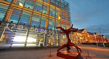 Een modern gebouw met een glazen gevel en een sculptuur van een rode figuur in een dynamische pose.