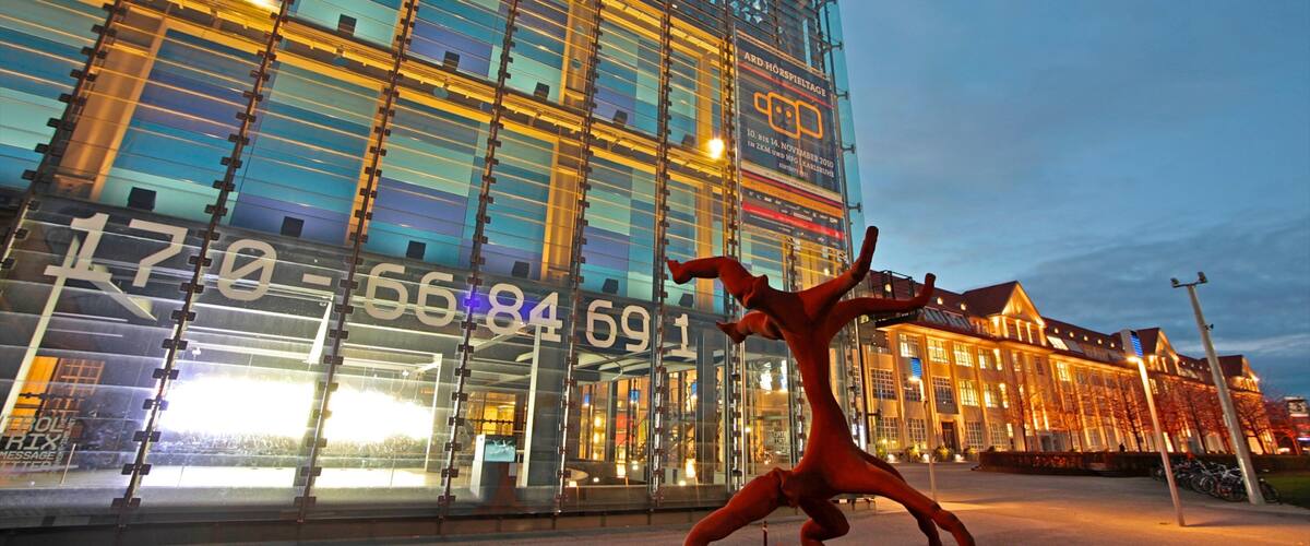 A modern building with a glass facade and a sculpture of a red figure in a dynamic pose.