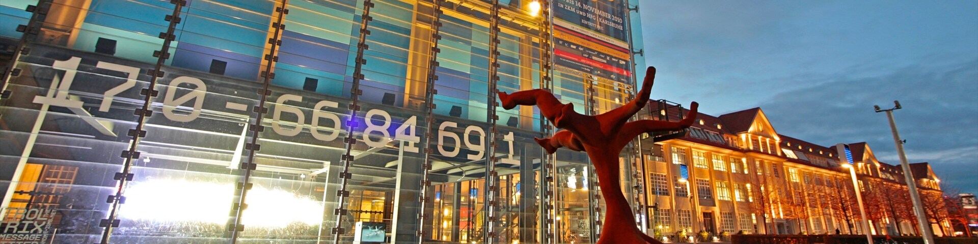 A modern building with a glass facade and a sculpture of a red figure in a dynamic pose.