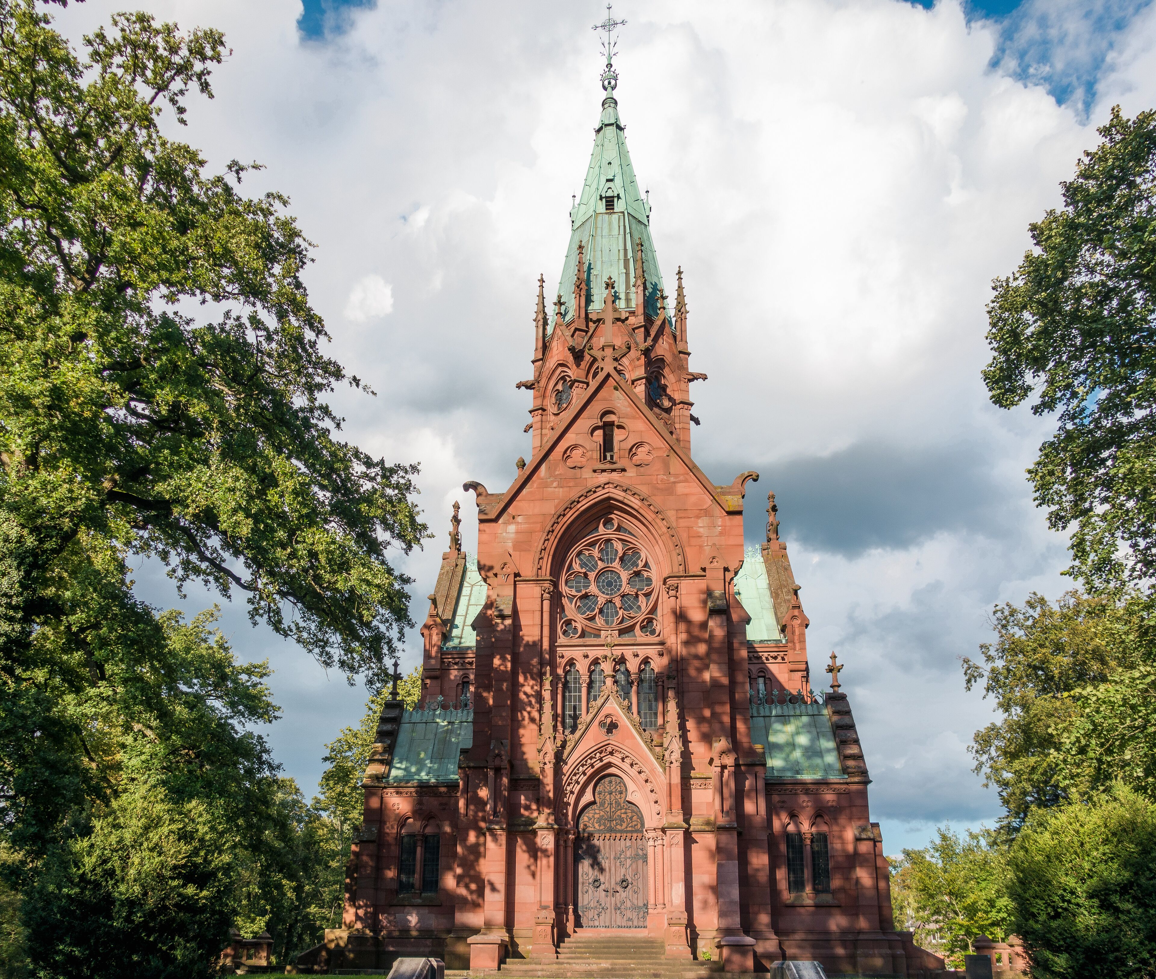 A large red brick church with a tall spire and a large rose window.