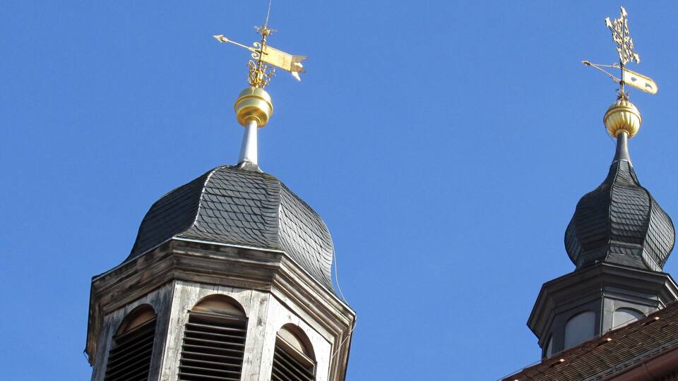 Two church domes with golden weather vanes against a clear blue sky.