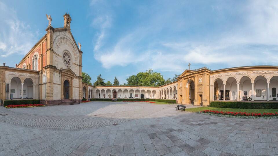 A grand courtyard with a central building featuring a tall tower and arched walkways.