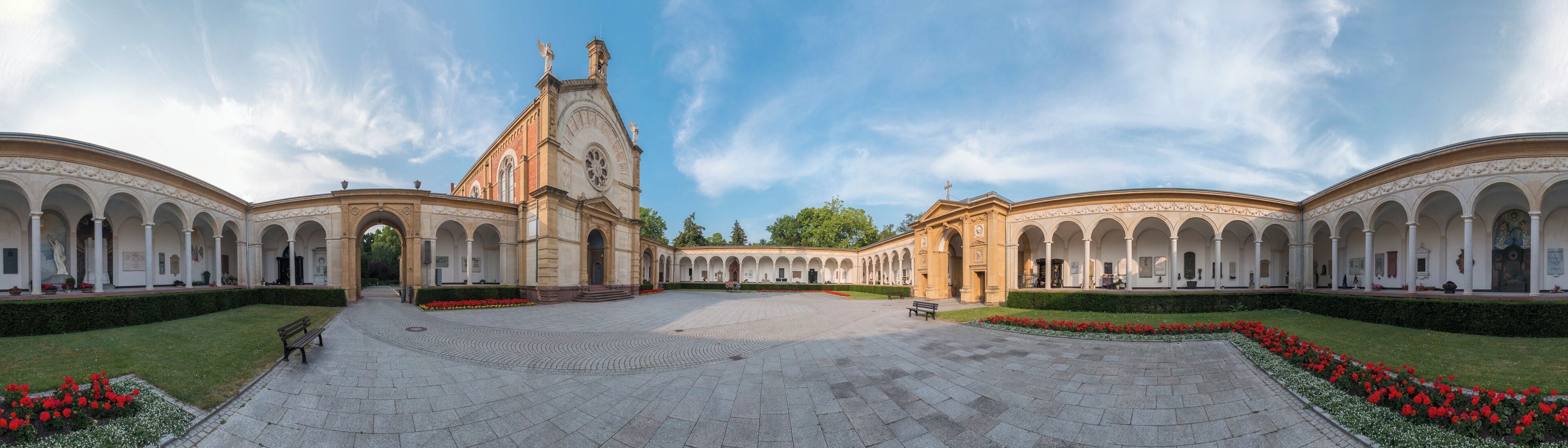 A grand courtyard with a central building featuring a tall tower and arched walkways.
