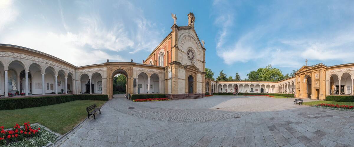 A grand courtyard with a central building featuring a tall tower and arched walkways.