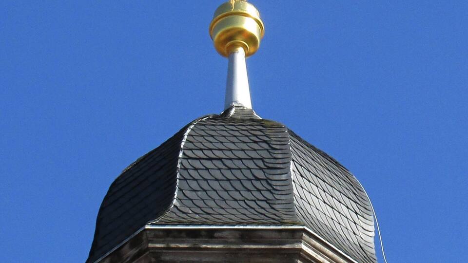 A weather vane atop a building with a dome and arched windows.
