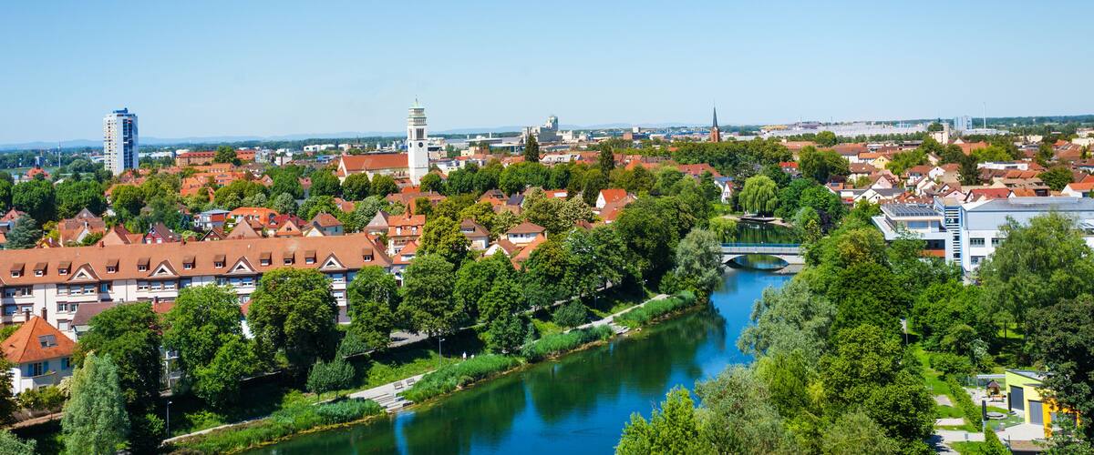 A river flowing through a town with red-roofed buildings and a prominent tower.