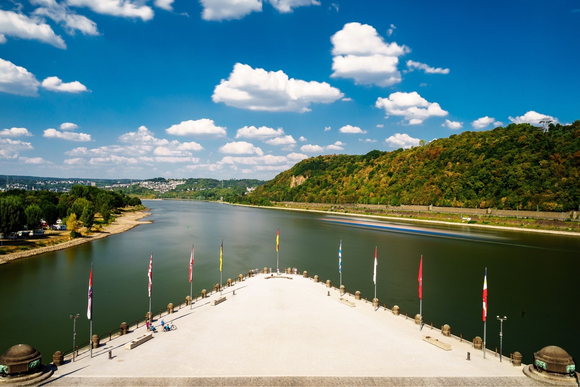 Un río con banderas, un puente y una colina con árboles.