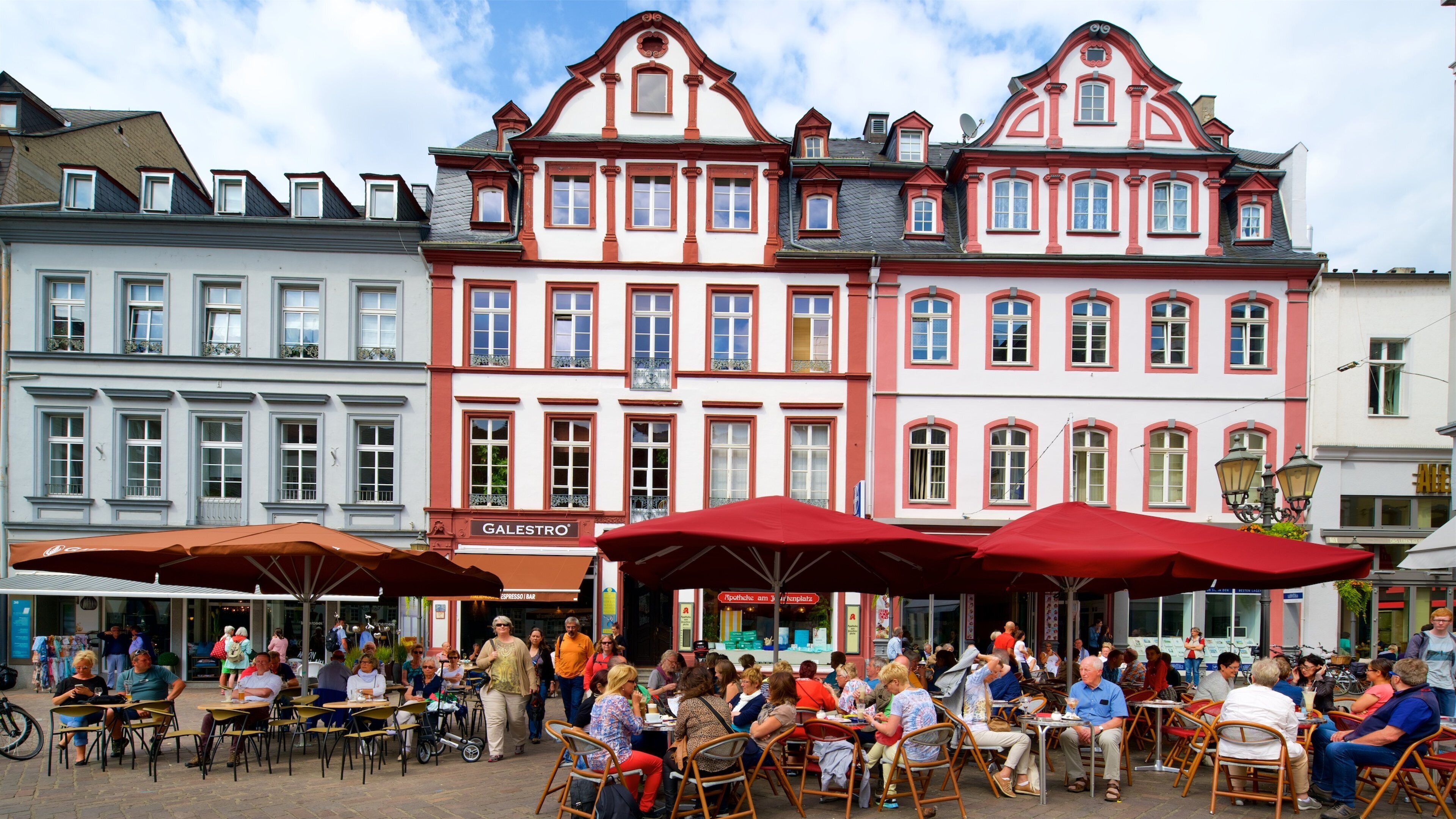 A bustling outdoor café with red umbrellas and people dining.