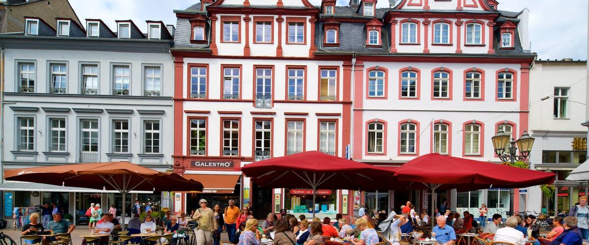 A bustling outdoor café with red umbrellas and people dining.