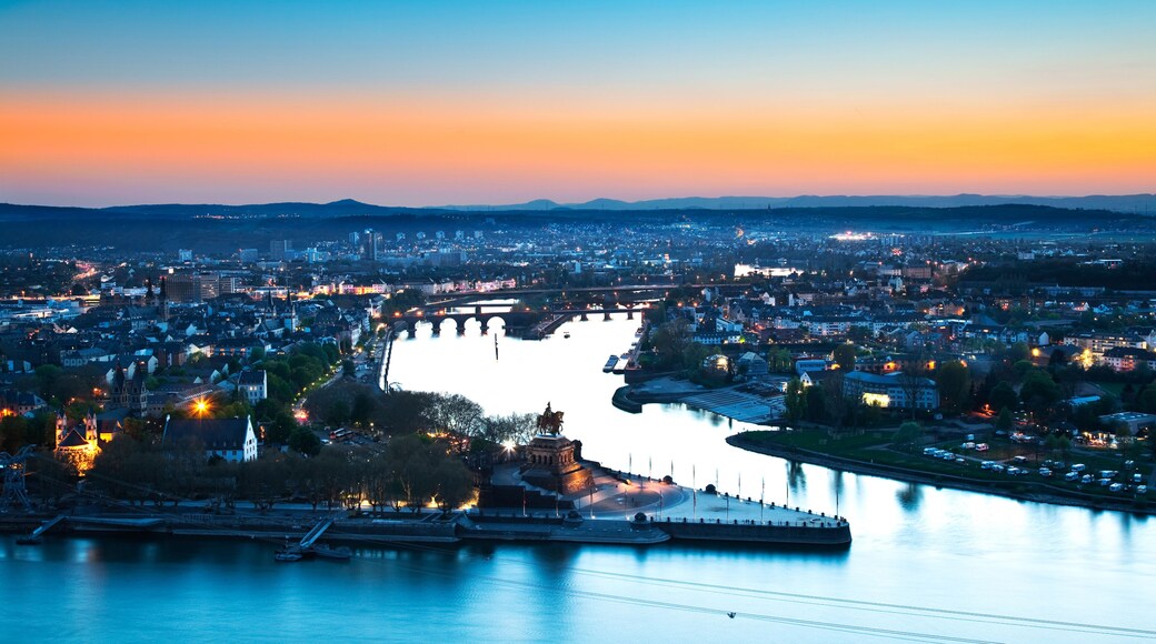 A cityscape at dusk with a river, bridges, and a prominent statue.