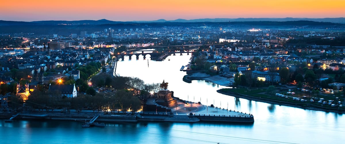 Un paisaje urbano al atardecer con un río, puentes y una estatua destacada.