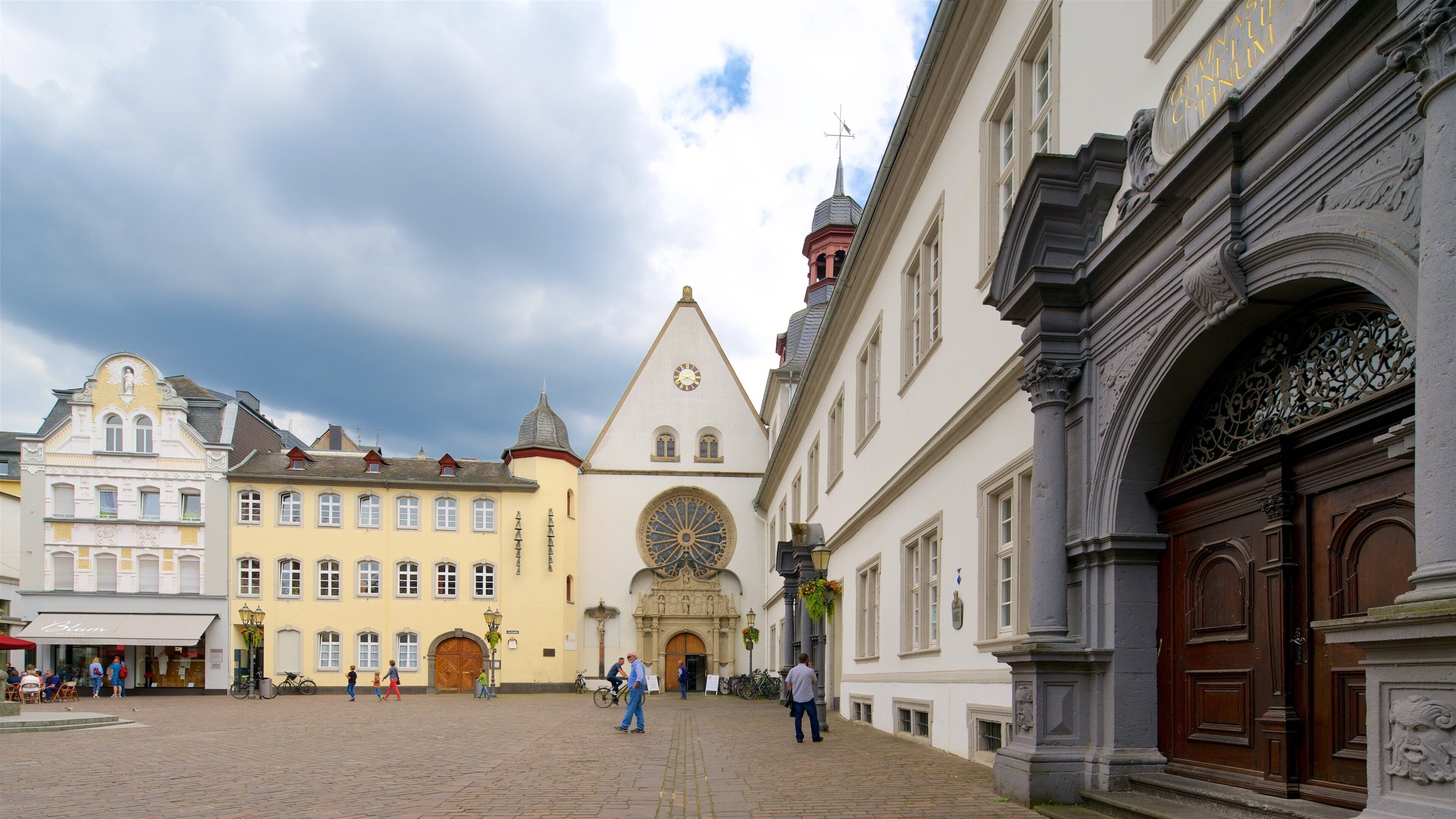 A cobblestone square with historic buildings, a church with a clock tower, and a large ornate door.