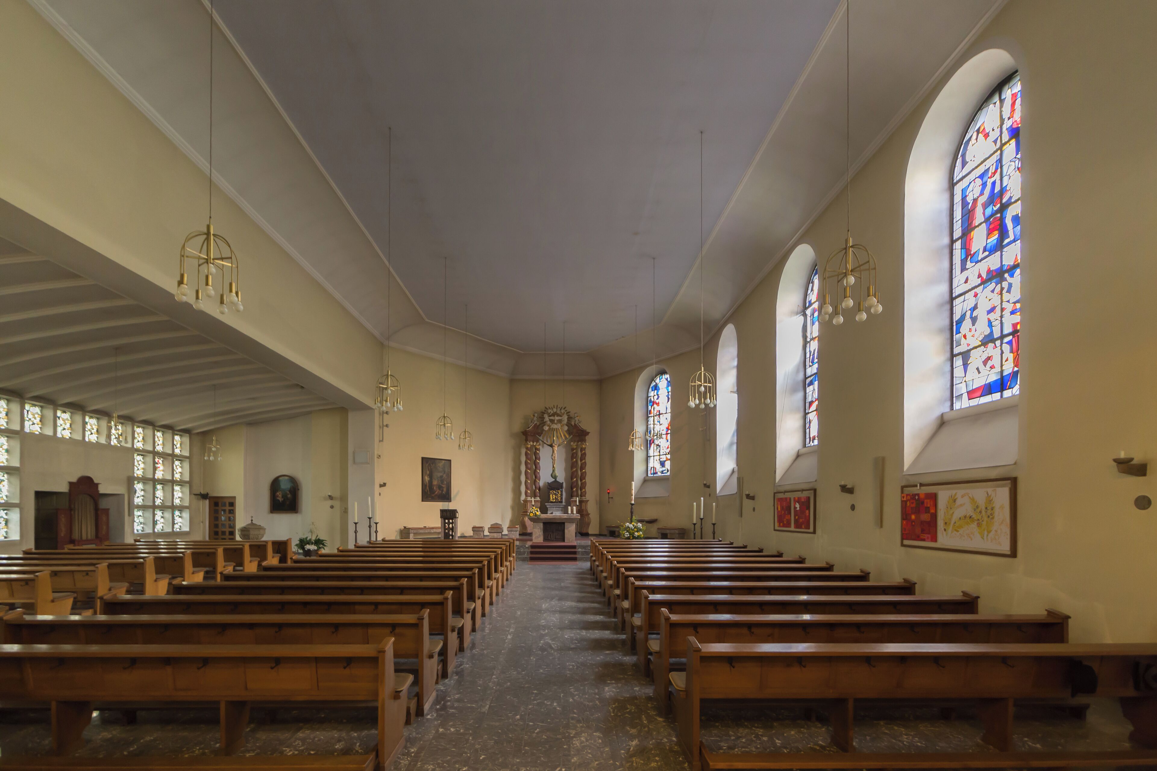 A church interior with wooden pews, stained glass windows, and a central altar.