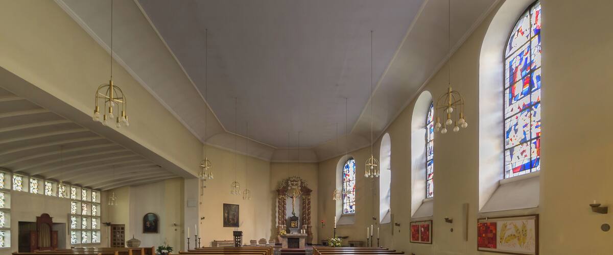 A church interior with wooden pews, stained glass windows, and a central altar.
