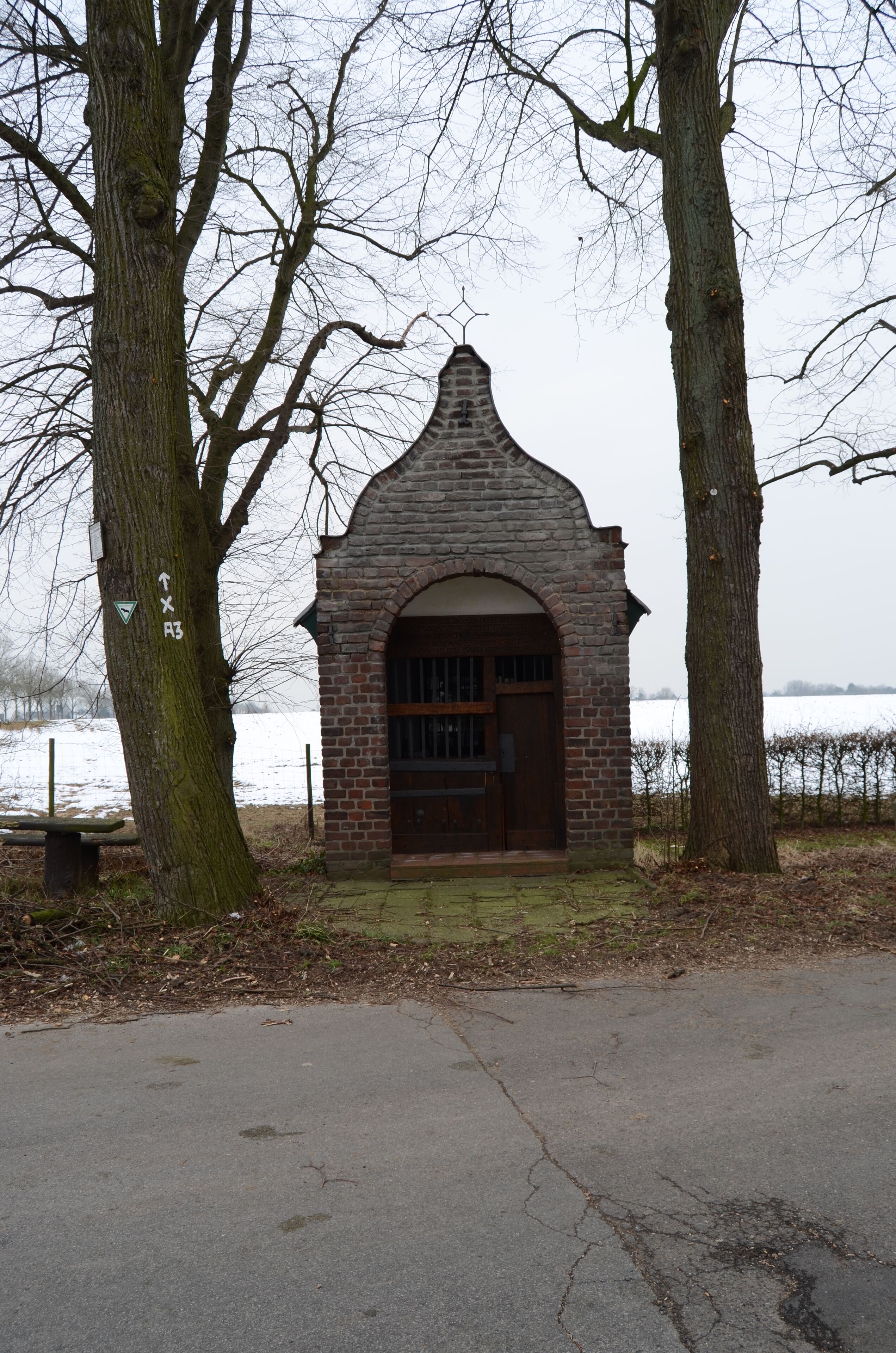 A small brick structure with a pointed roof, surrounded by trees and a body of water in the background.