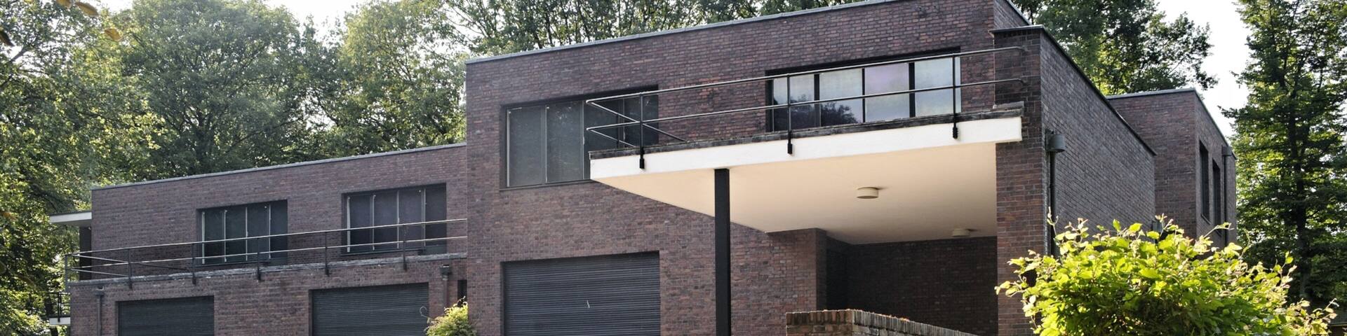 A modern two-story house with brick walls, large windows, and a small balcony.
