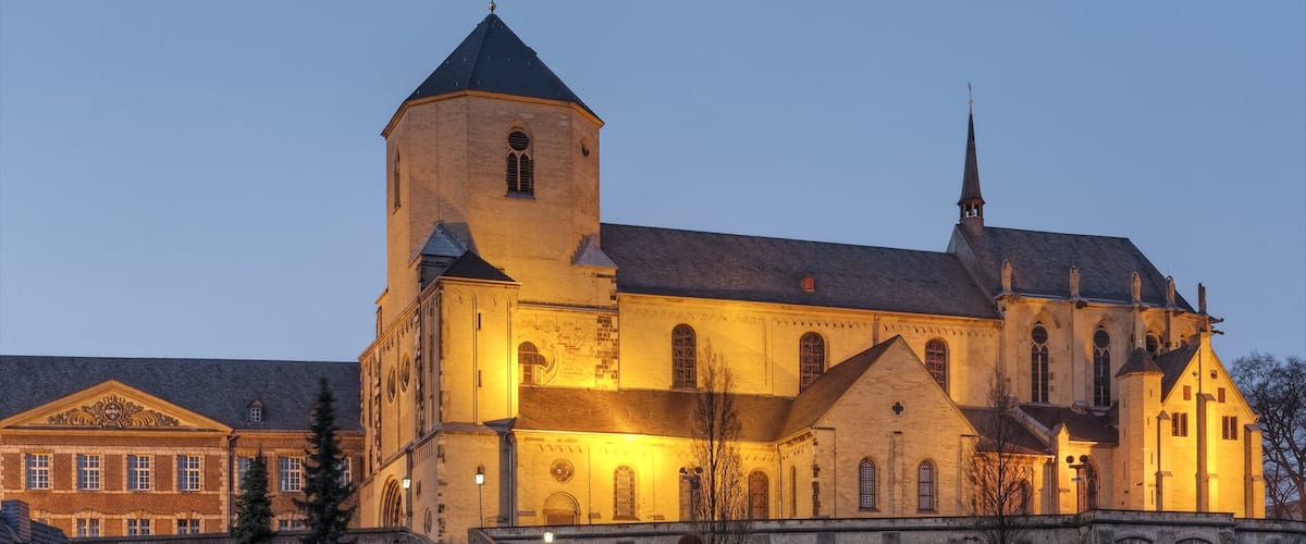 A large church with a prominent tower and a spire, illuminated at dusk.