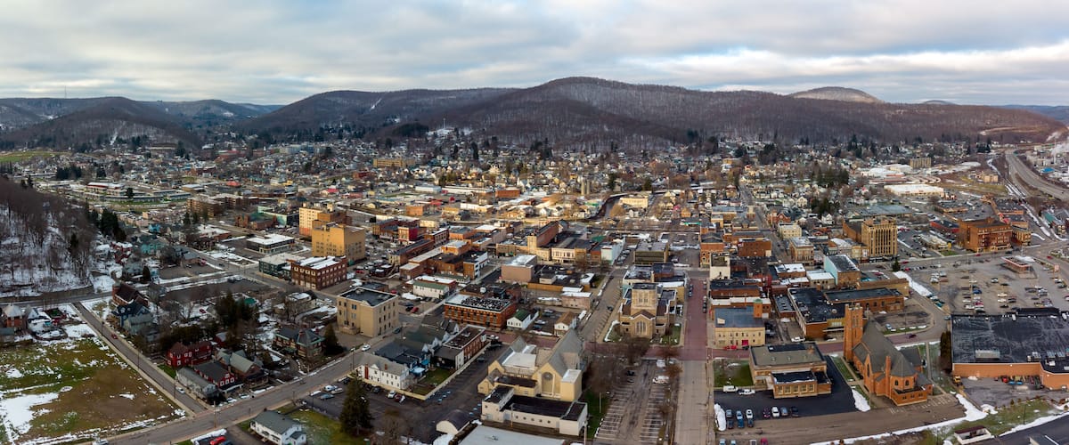 Paisagem urbana com mistura de edifícios históricos e modernos, cercada por montanhas e um céu nublado.